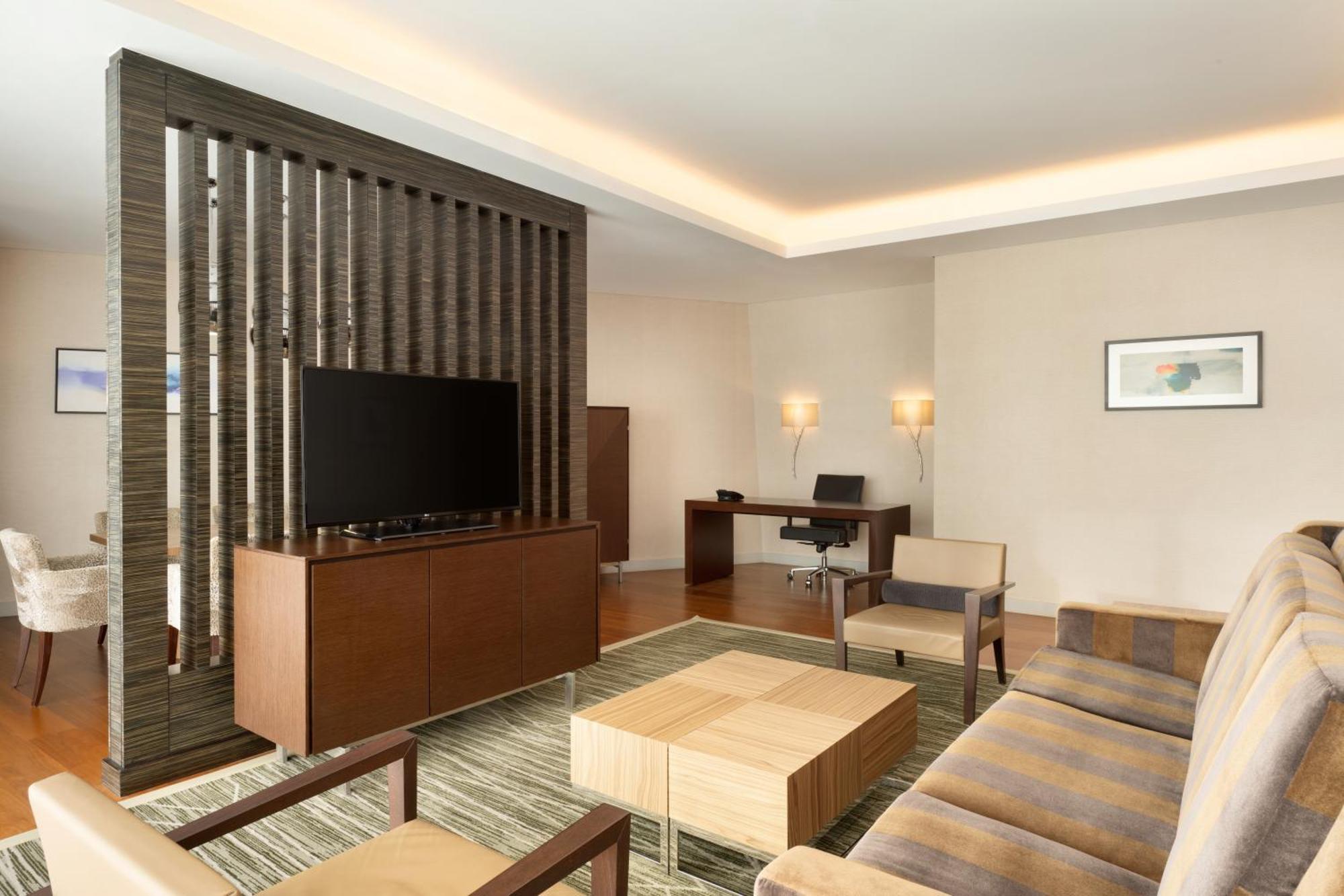 Hilton Riyadh Hotel & Residences Eksteriør billede The photo shows a modern living space that features a contemporary design. It includes a seating area with a beige sofa and two armchairs arranged around a square wooden coffee table. A wall-mounted flat-screen TV is positioned on a decorative wooden