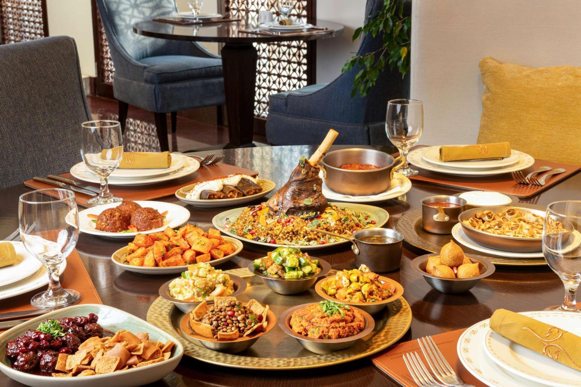 Hilton Riyadh Hotel & Residences Eksteriør billede The photo depicts a beautifully arranged dining table featuring a variety of dishes. There are several large plates filled with different foods, including a prominent dish at the center that appears to be rice and meat, likely a type of biryani or pi